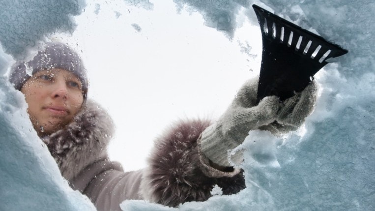 Person removing snow on windshield of a car.