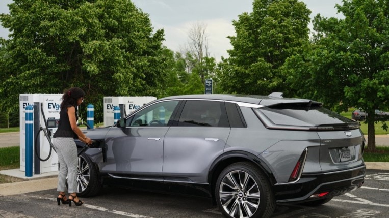 A woman charges a Cadillac Lyriq electric vehicle at a GM-branded public charging station