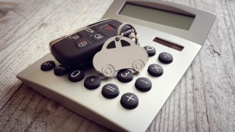 A car-shaped key ring and a car's key fob sit on a calculator.