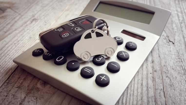A car-shaped key ring and a car's key fob sit on a calculator.