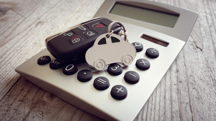 A car-shaped key ring and a car's key fob sit on a calculator.