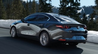 Grey 2023 Mazda3 driving near snow bank.