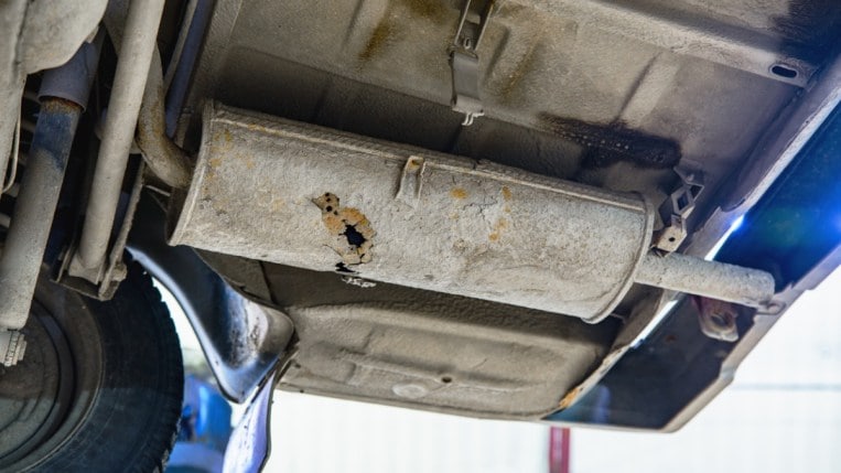 A rusted muffler underneath a vehicle. 