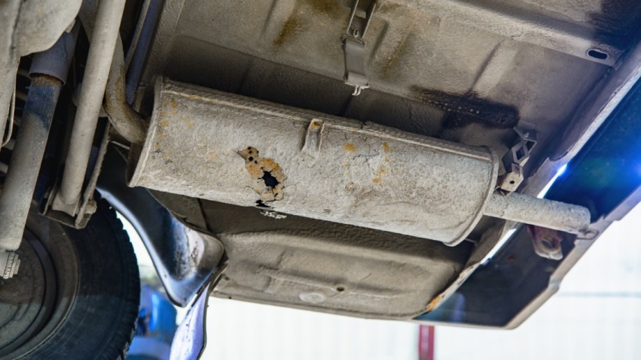 A rusted muffler underneath a vehicle. 