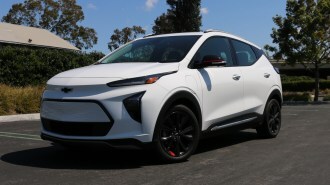 White 2023 Chevrolet Bolt EUV Premier near a green hedge.
