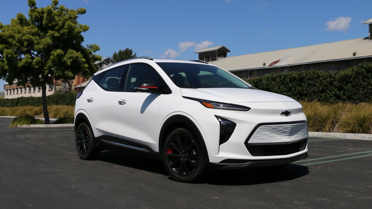 White 2023 Chevrolet Bolt EUV Premier near a tree and green hedge.