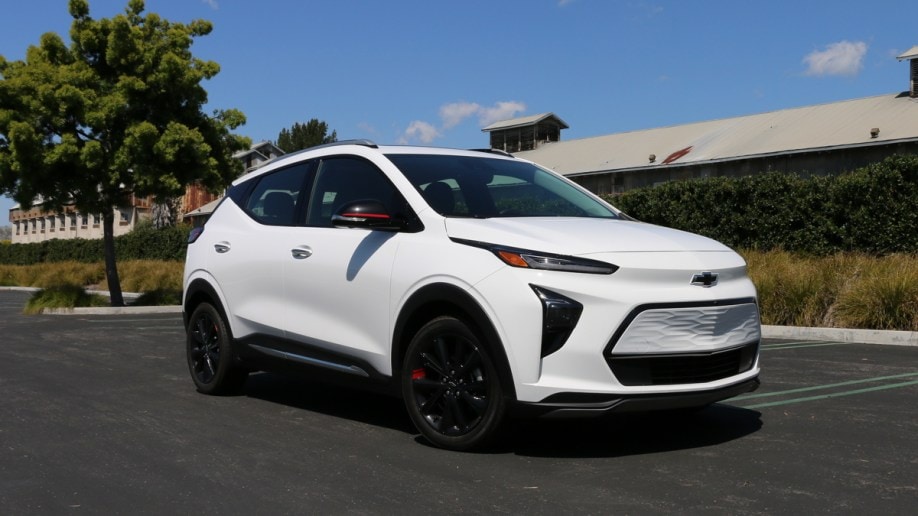 White 2023 Chevrolet Bolt EUV Premier near a tree and green hedge.