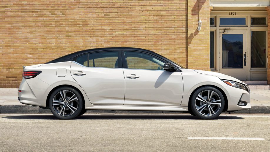 White 2023 Nissan Sentra profile near brick building.