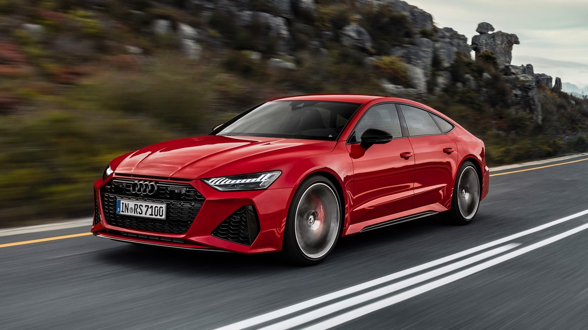 Red 2021 Audi RS7 Sportback with dynamic all-wheel steering driving on a road near rocks.