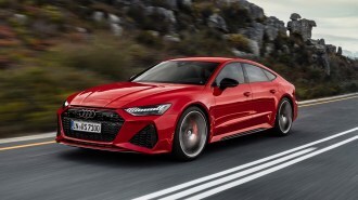 Red 2021 Audi RS7 Sportback with dynamic all-wheel steering driving on a road near rocks.