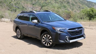 Blue 2023 Subaru Outback Touring with green hills in the background.