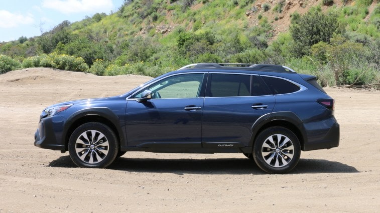 Blue 2023 Subaru Outback Touring profile on a dirt road.