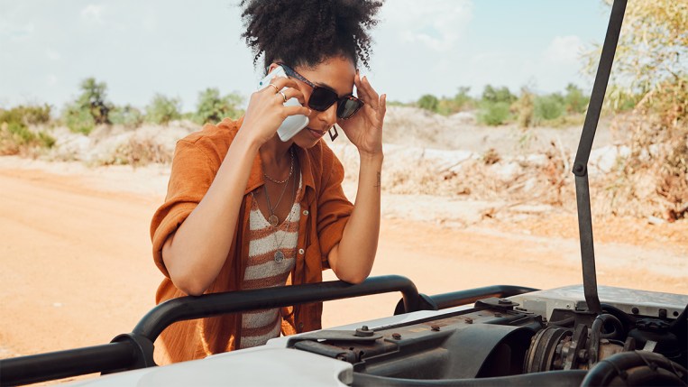 woman on the phone looking at her broken down car