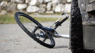 A bicycle lies in the road in front of a stopped car