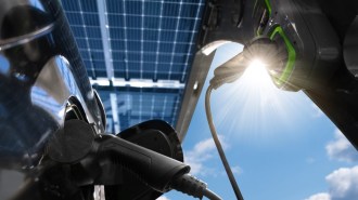 A closeup of an electric vehicle charger silhouetted against the glare of the sun