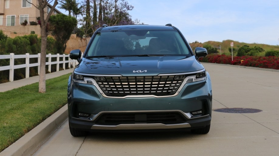 2023 Kia Carnival in blue front view near white fence.