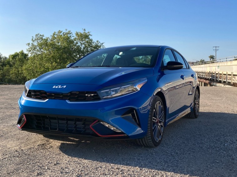 2023 Kia Forte GT in blue near a concrete bridge.