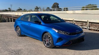 2023 Kia Forte GT in blue near a concrete bridge.