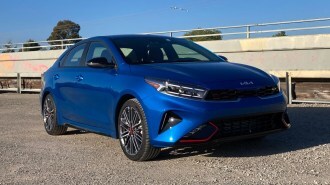 2023 Kia Forte GT in blue near a concrete bridge.