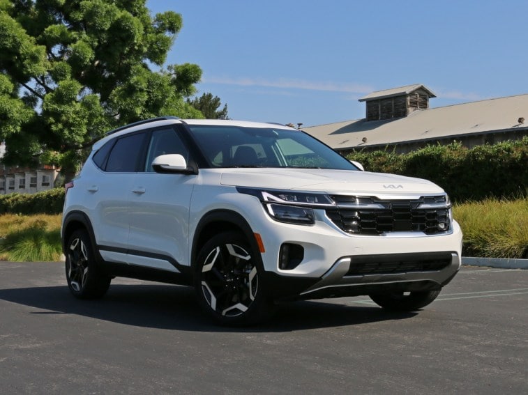 2024 Kia Seltos SX in white near green hedge and grass.