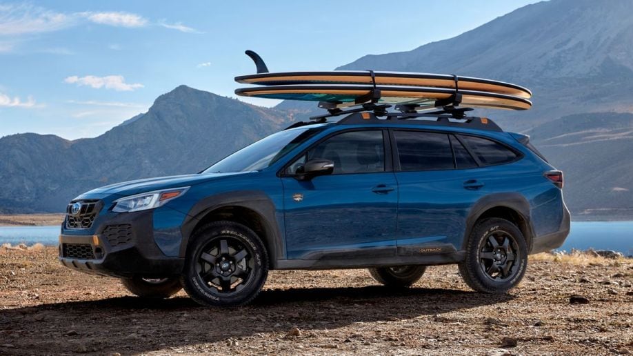 2024 Subaru Outback in blue near a lake with surfboards on the roof.
