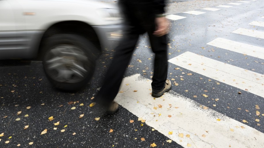 A car perilously close to a pedestrian in a pedestrian crossing