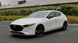 2024 Mazda3 Hatchback in white next to grass and bushes.