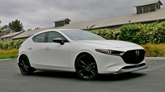 2024 Mazda3 Hatchback in white next to a long barn.