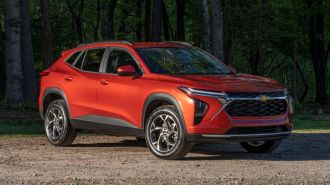 2024 Chevrolet Trax LT in Cayenne Orange Metallic parked on a gravel road in front of trees.