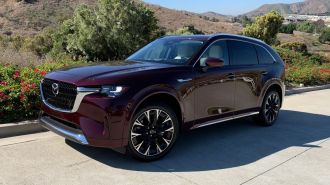 2024 Mazda CX-90 Turbo in Artisan Red in red near bushes.