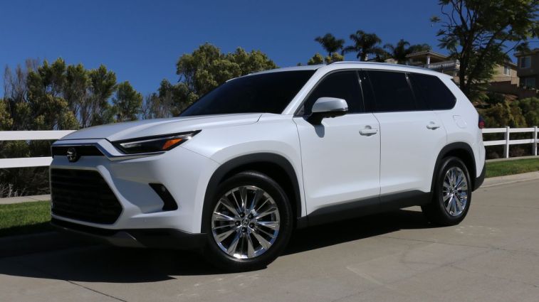 2024 Toyota Grand Highlander in white with a fence in the background.