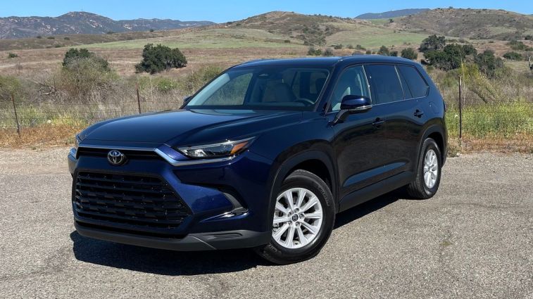 2024 Toyota Grand Highlander Hybrid in blue with hills in the background.