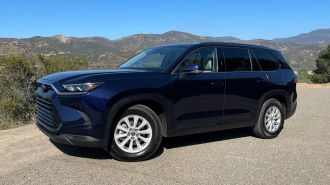2024 Toyota Grand Highlander Hybrid in blue with hills in the background.