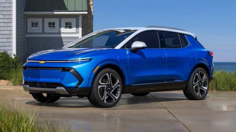 2024 Chevrolet Equinox EV 3LT in Riptide Blue parked beside a lakeside home.