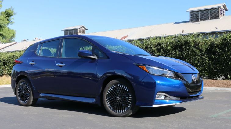 2024 Nissan Leaf SV in blue with a green hedge in the background.