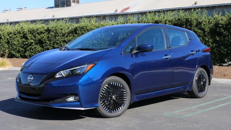 2024 Nissan Leaf SV in blue with a green hedge in the background.