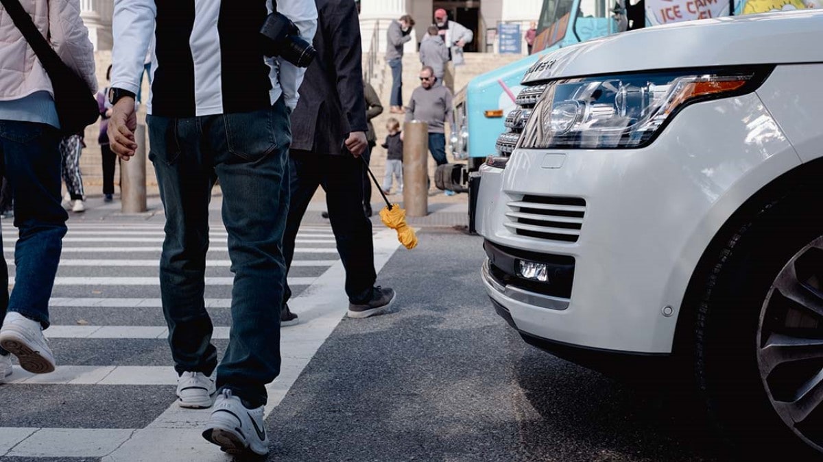 Pedestrians walk in front of an SUV