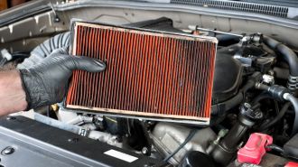 A dirty air filter held over a car engine during general auto maintenance.