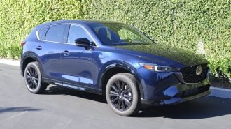 2024 Mazda CX-5 Turbo in blue near an ivy green wall.
