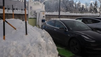 A Tesla Model 3 plugged into a public charger in heavy snow