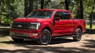 2024 Ford F-150 Lariat in red with trees in the background.
