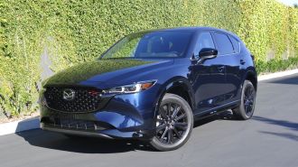 2024 Mazda CX-5 Turbo in blue parked near an ivy wall.