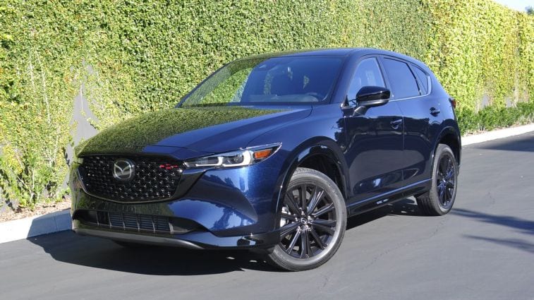 2024 Mazda CX-5 Turbo in blue parked near an ivy wall.