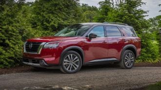 2024 Nissan Pathfinder in red parked on gravel near trees.
