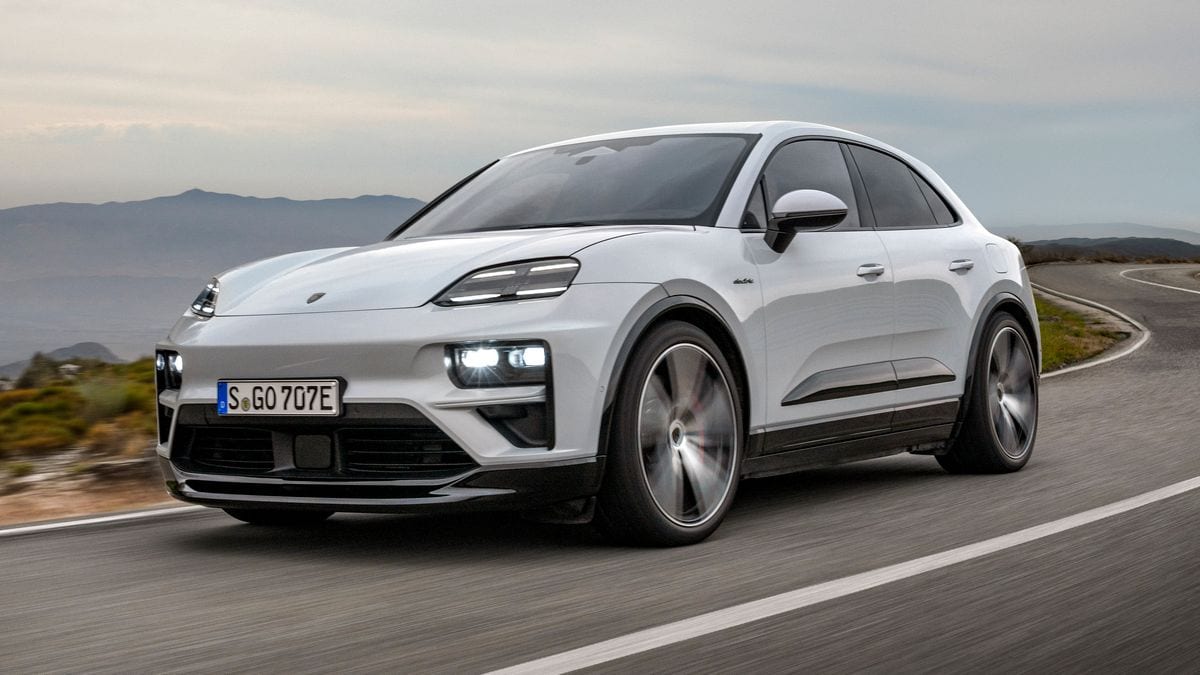 2025 Porsche Macan Turbo EV in white driving down a curvy road.