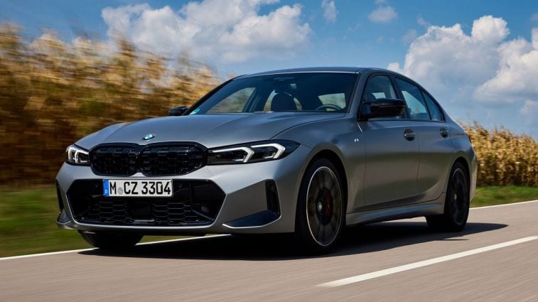 A silver 2024 BMW M340i driving down a road near a corn field.