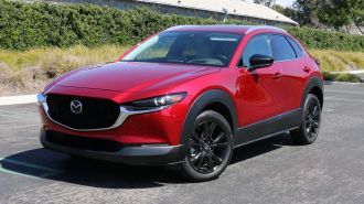 2024 Mazda CX-30 in red with bushes and a barn in the background.