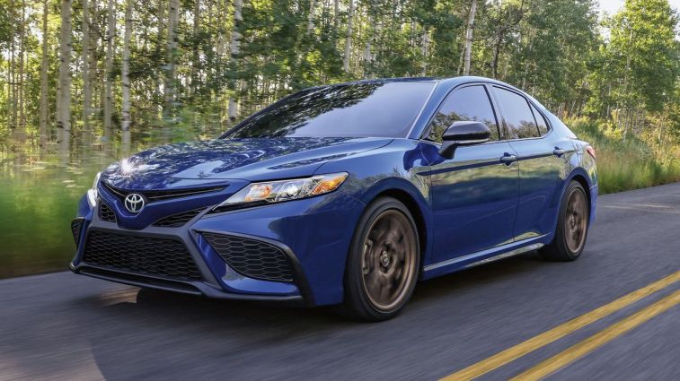 2024 Toyota Camry SE Nightshade in blue driving by trees.