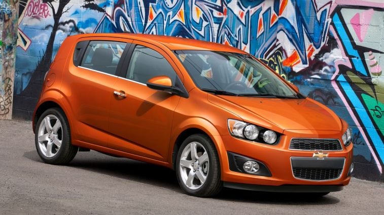 2012 Chevrolet Sonic LTZ Hatchback Inferno Orange parked near a wall of graffiti.