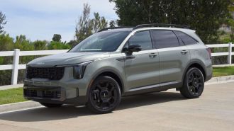 2024 Kia Sorento X-Line in Jungle Green with a white fence in the background.